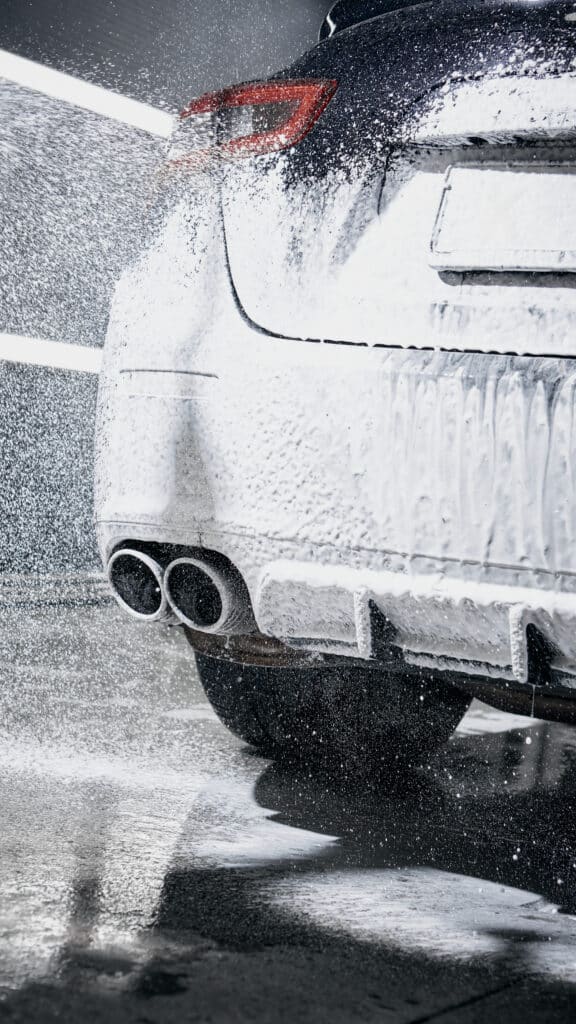 Mousse et Eau sur Arrière de Voiture Sport Lavage haute pression d'une voiture recouverte de mousse blanche, mettant en évidence les doubles sorties d'échappement arrière.
